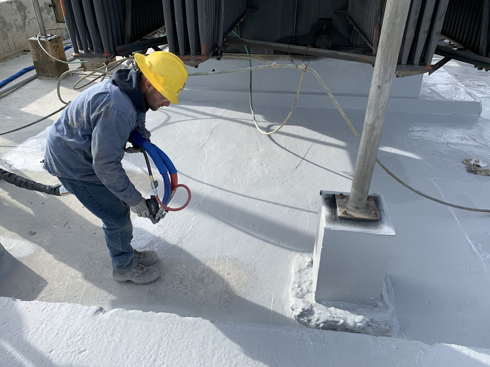 Liner technician sprays a concrete pad beneath a large storage tank with polyurea spray liner for secondary containment